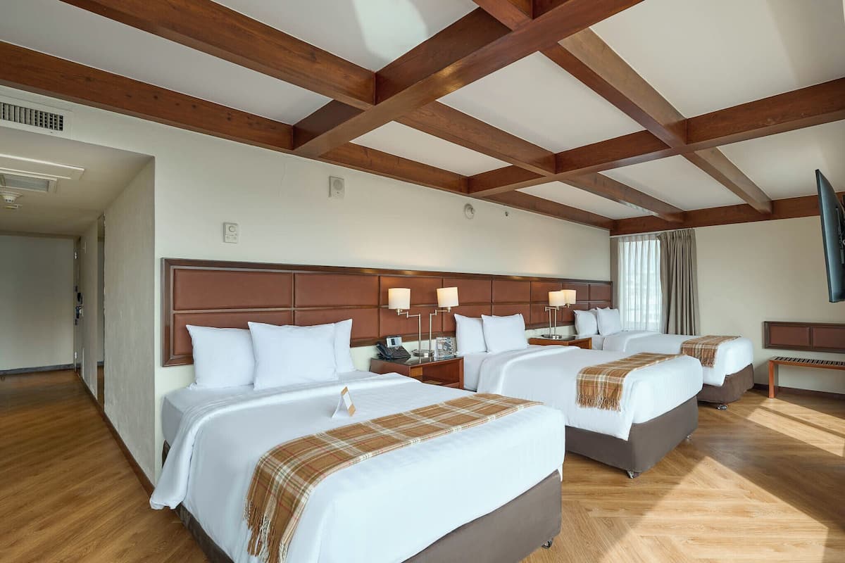 Une chambre d’hôtel avec deux lits, des poutres apparentes au plafond, un téléviseur à écran plat et une fenêtre avec des rideaux.