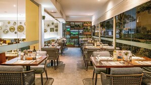 Un restaurante con varias mesas y sillas, un ventanal con plantas y vistas al exterior.