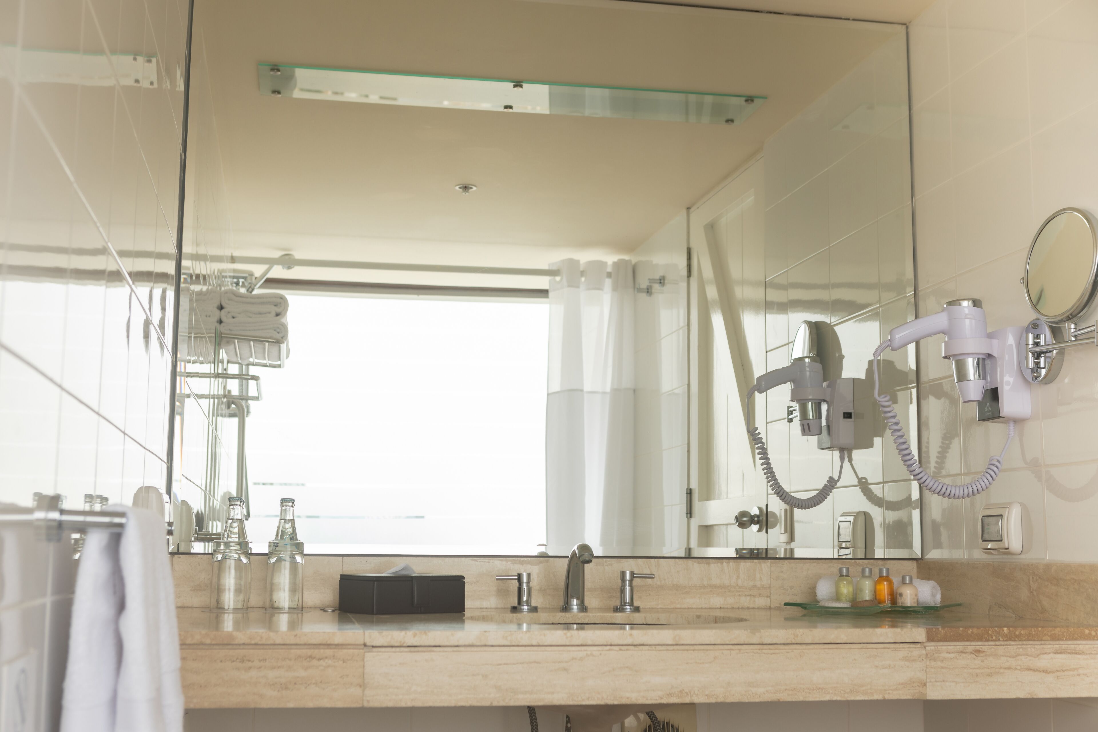 A modern bathroom with a large mirror, a glass shower enclosure, and a vanity with a sink and toiletries.