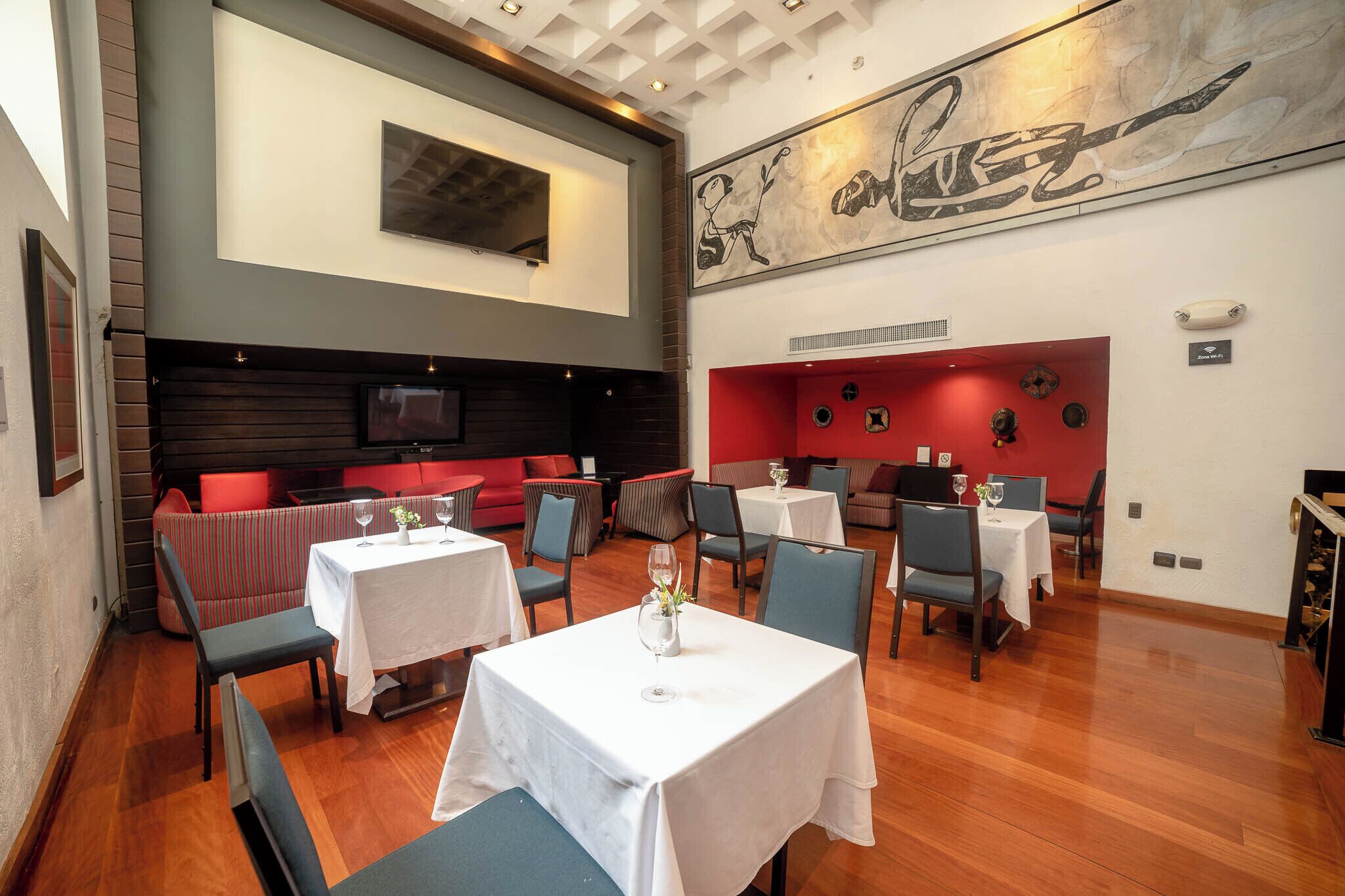 Un restaurante con varias mesas y cabinas, una gran obra de arte en la pared y un televisor montado.