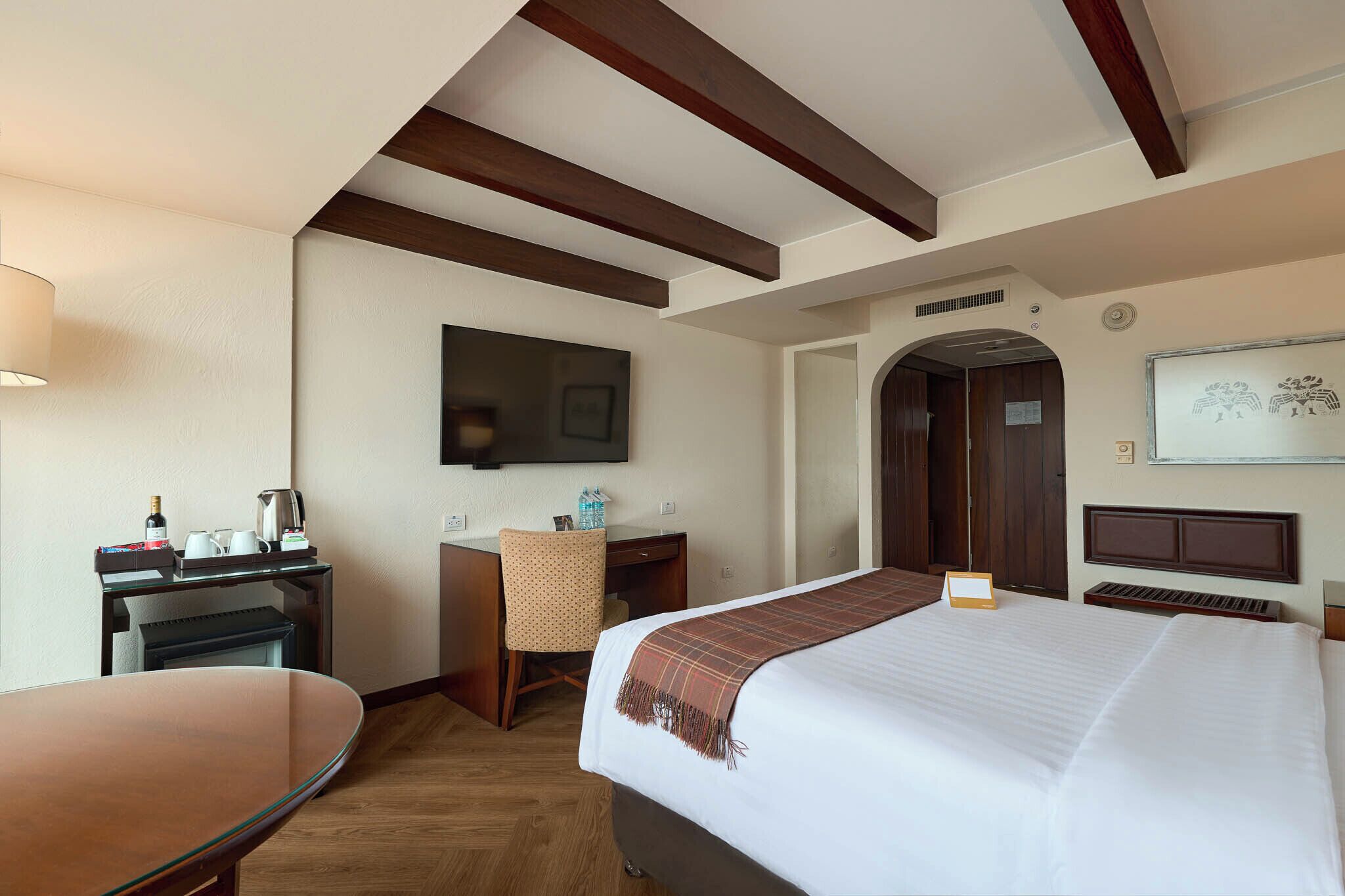 Habitación de hotel con cama, escritorio, silla y televisor en la pared.