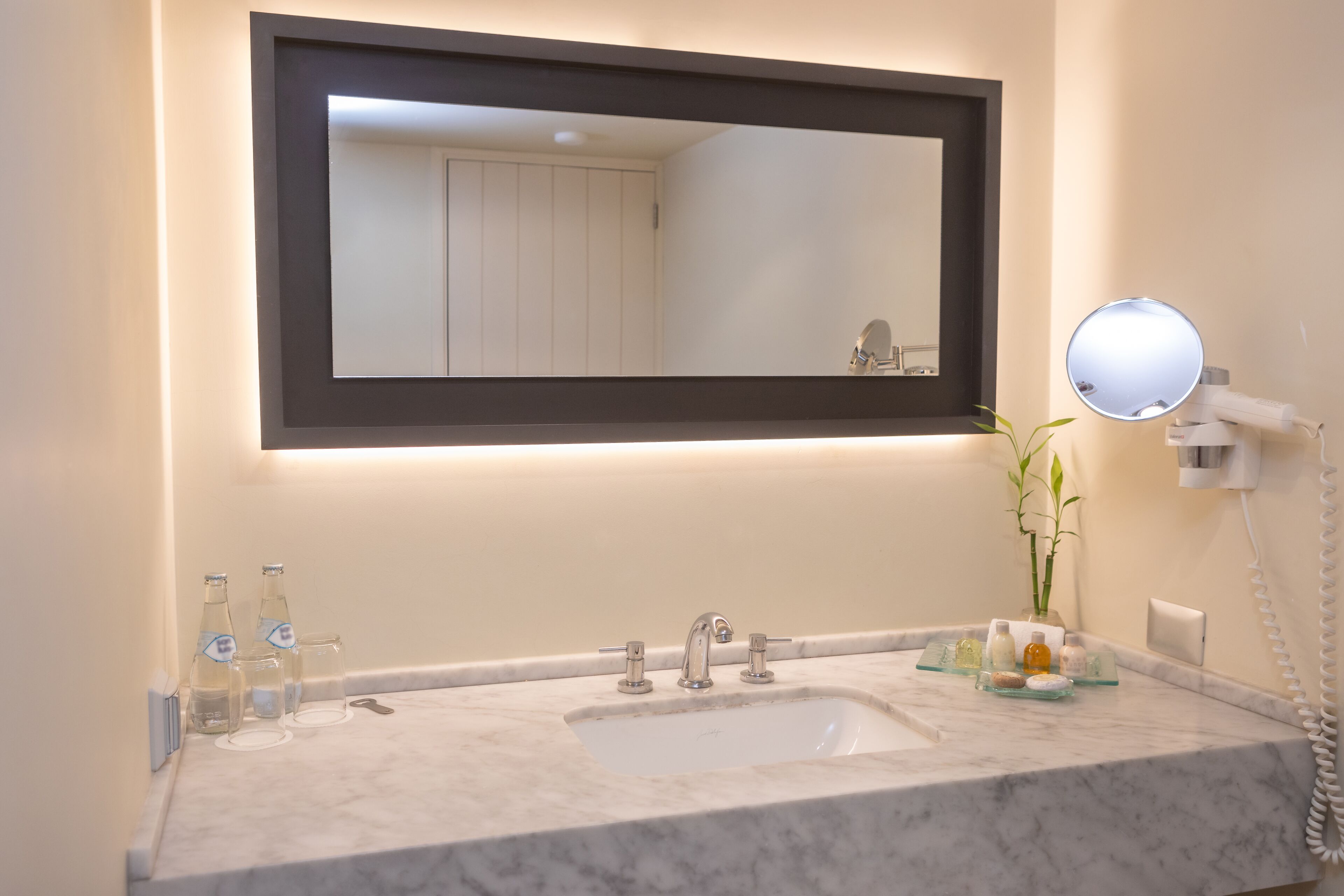 A bathroom with a large mirror, a sink, and a round mirror on the wall.