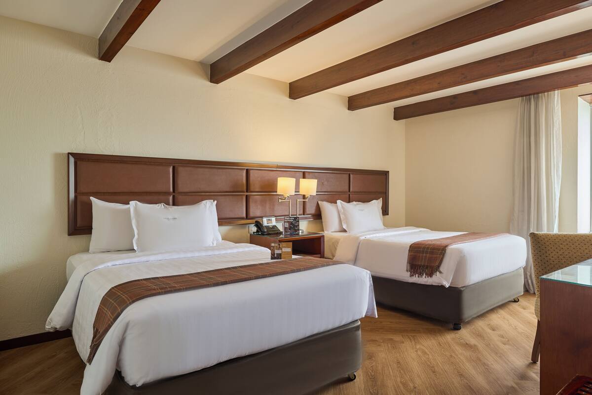 Une chambre d’hôtel avec deux lits, un plafond en bois, une table de chevet avec des lampes et une chaise.