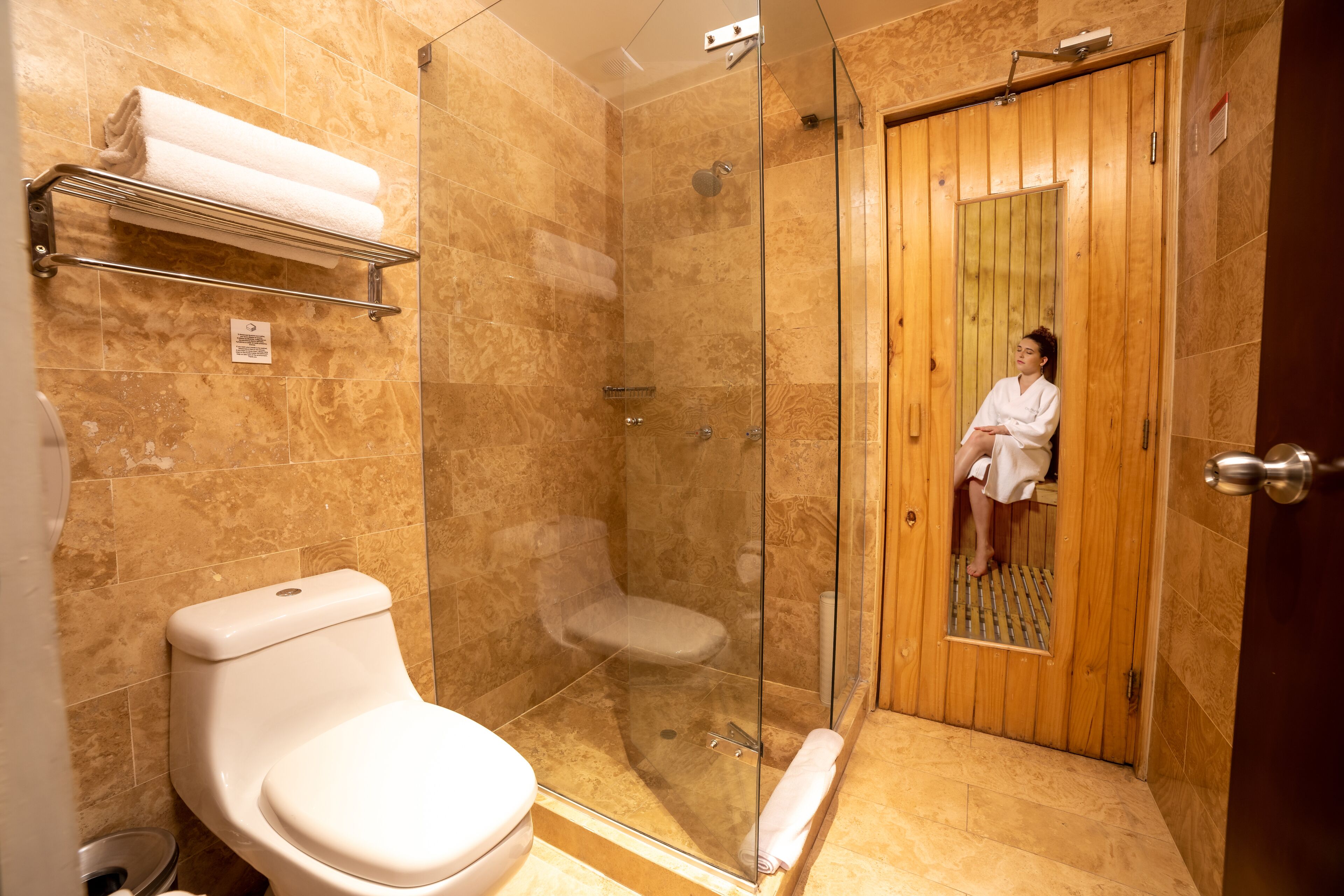 Un baño con ducha de vidrio, inodoro y puerta de madera.