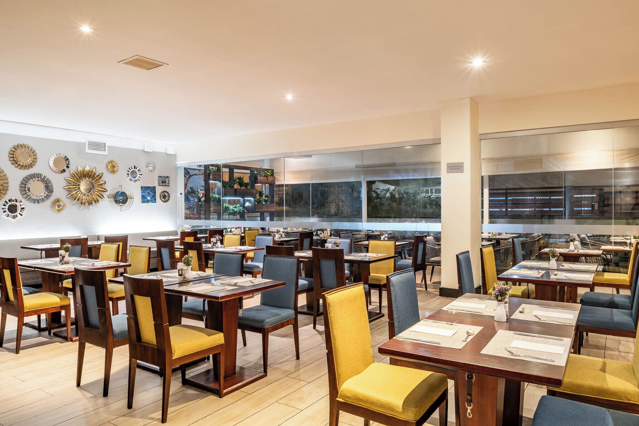 Un restaurante espacioso con numerosas mesas y sillas, amplias ventanas y decoración mural.