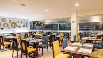 Un restaurante espacioso con numerosas mesas y sillas, amplias ventanas y decoración mural.