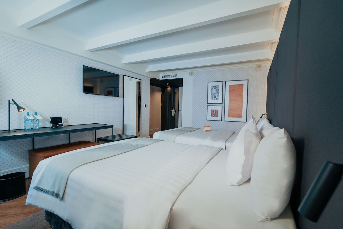 Une chambre d’hôtel moderne, dotée d’un grand lit, d’un bureau avec un ordinateur, d’un miroir et de tableaux encadrés accrochés au mur.