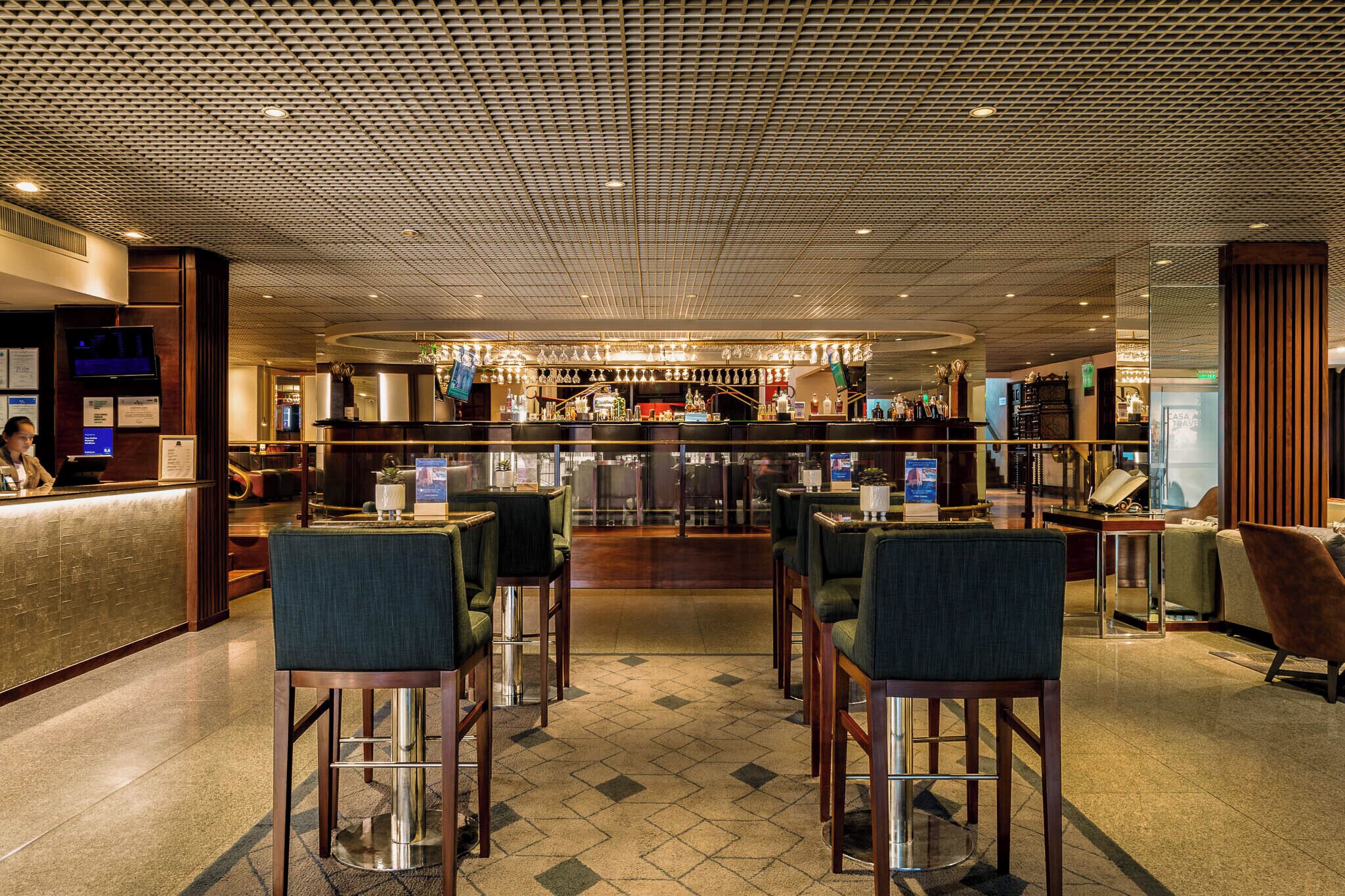 Un vestíbulo de hotel con zona de bar, asientos y mostrador de recepción.