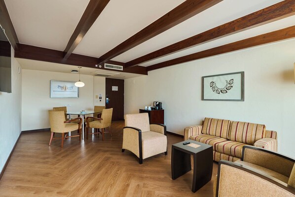 Una sala de estar con vigas de madera, un sofá, sillones, una mesa de centro y un comedor con sillas y una mesa.