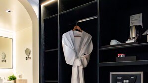 Un baño moderno con suelo de madera, un tocador negro con espejo, una bata colgada en un perchero y un refrigerador empotrado con bebidas.