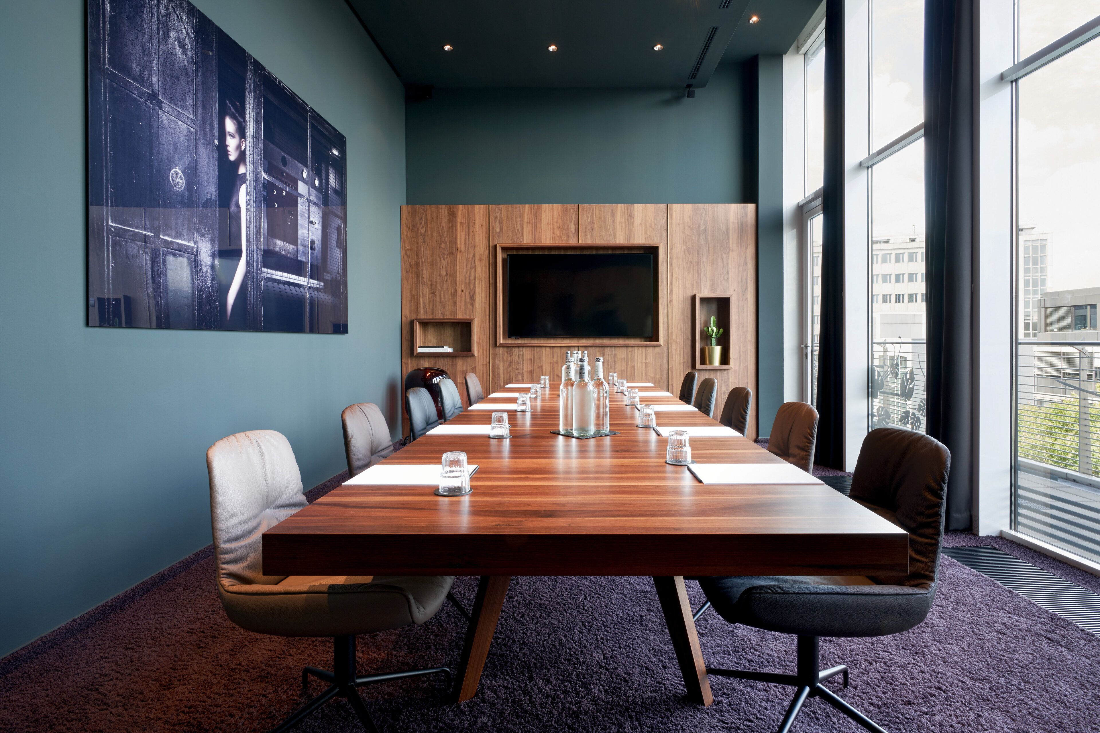Una sala de conferencias con una larga mesa de madera, numerosas sillas, un televisor de pantalla plana grande y vistas de la ciudad a través de amplias ventanas.
