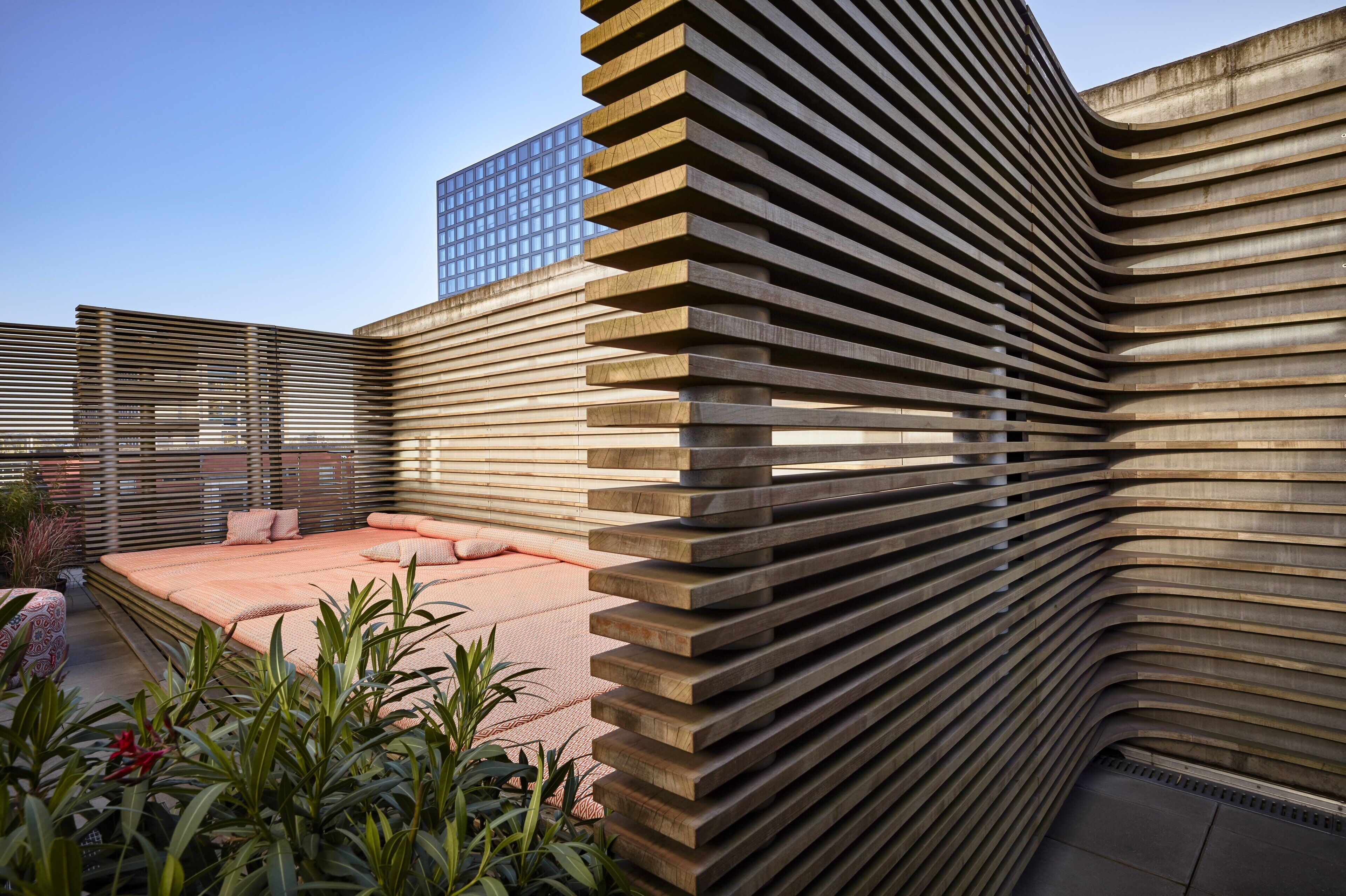 Un edificio moderno con fachada curva y jardín en la azotea con zona de estar.