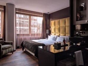 A hotel room with a large bed, a bedside table, a mirror, and a view of the city through large windows. - Roomers Frankfurt Central, Autograph Collection (Frankfurt)