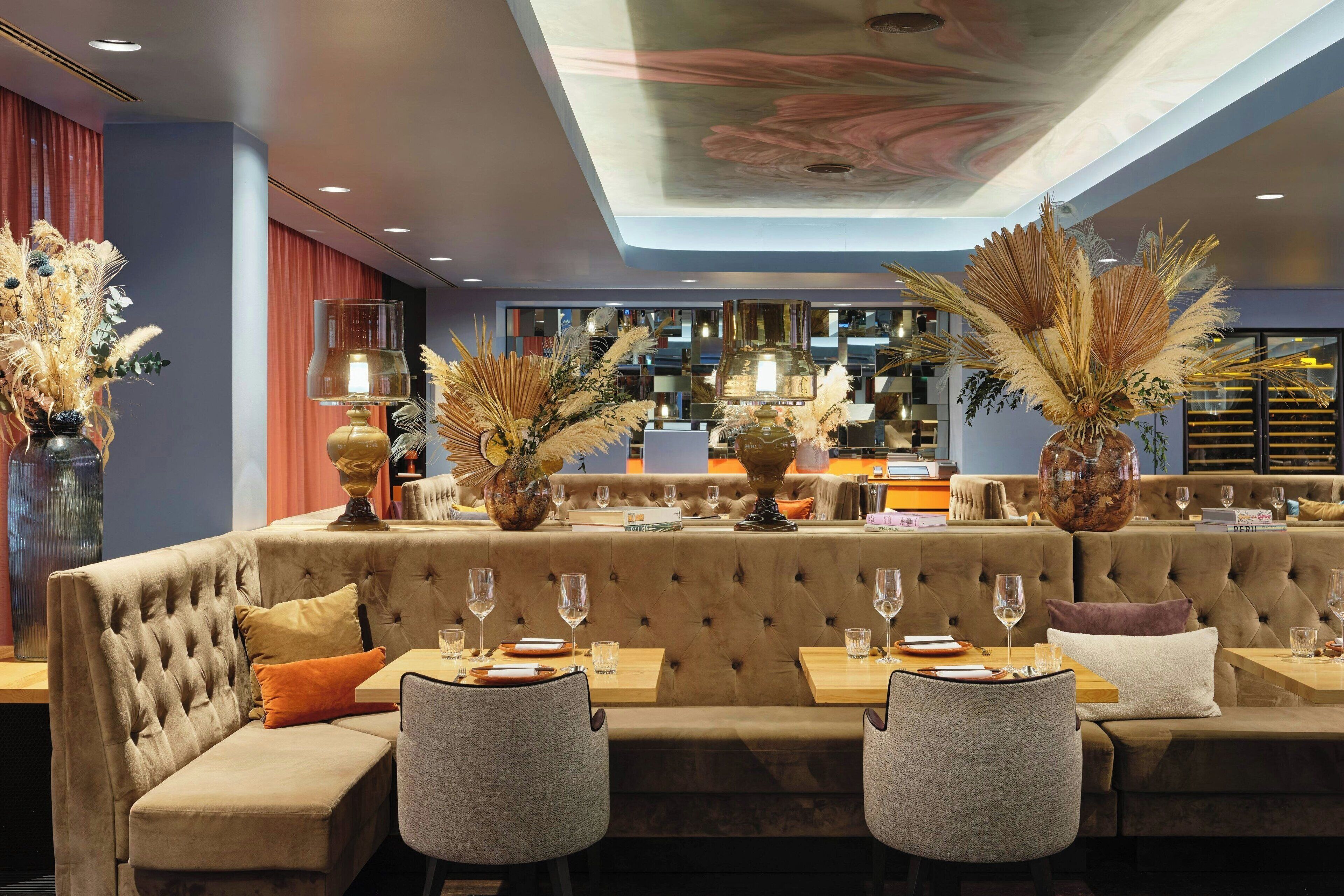 A modern restaurant with a plush seating area, tables set with wine glasses, and decorative plants.