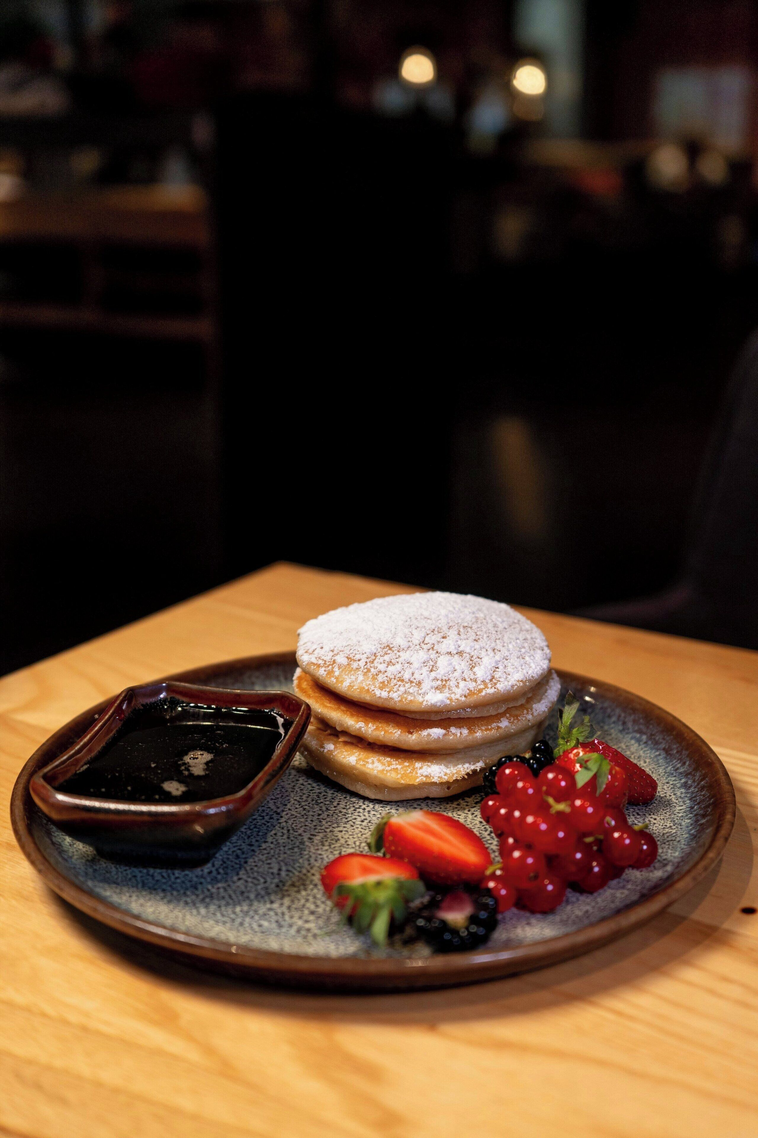 A plate with pancakes, berries, and a chocolate sauce.