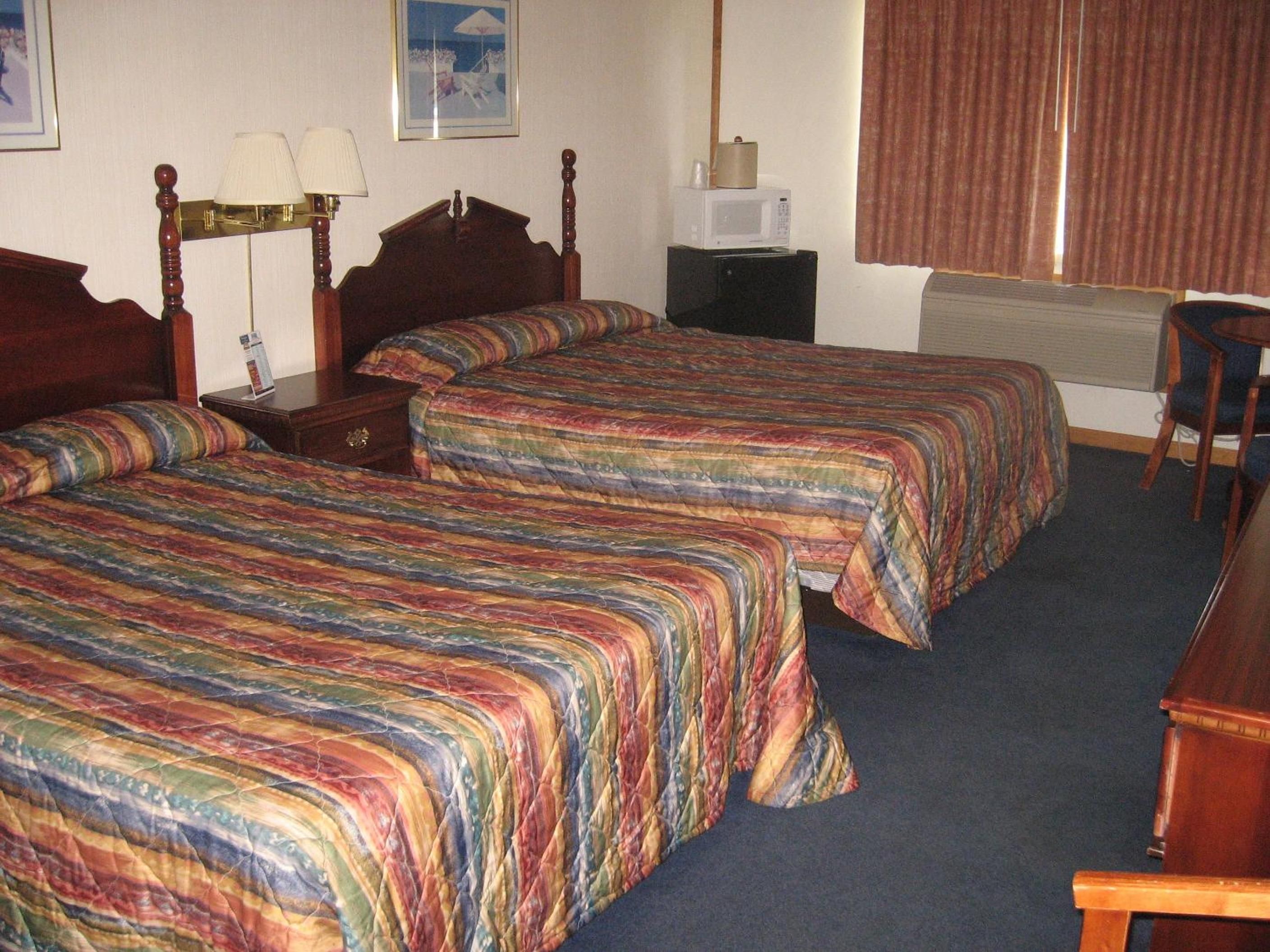 Ein Hotelzimmer mit zwei Betten, einem Schreibtisch, einem Stuhl, einer Mikrowelle und einer Lampe.