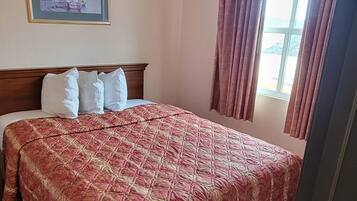 A hotel room with a large bed, a headboard, a framed picture on the wall, and a window with curtains.