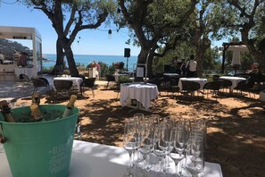 An outdoor dining area with tables and chairs, a bucket of champagne, and a view of the sea.