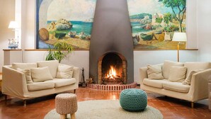 A living room with two beige sofas, a fireplace, and a large painting of a coastal scene. - Hotel Sant Roc (Palafrugell)