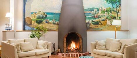 A living room with two beige sofas, a fireplace, and a large painting of a coastal scene.