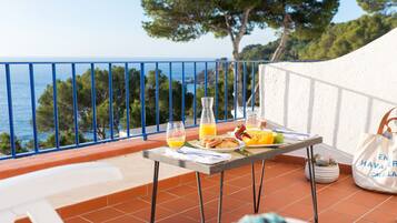 A balcony with a table set for breakfast, overlooking the sea.