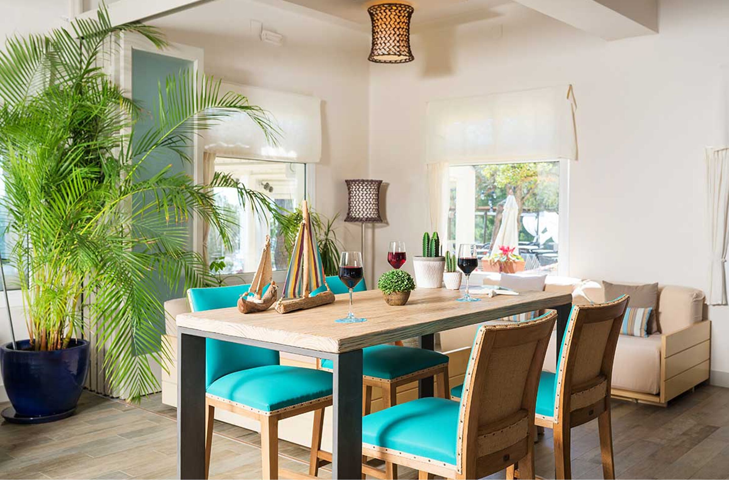 Un comedor con mesa de madera, sillas color turquesa y una planta grande en maceta.