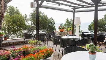 Un patio exterior con sillas y mesas de mimbre, plantas en macetas y vistas al mar.