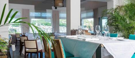 A restaurant with a table set for two, large windows, and indoor plants.