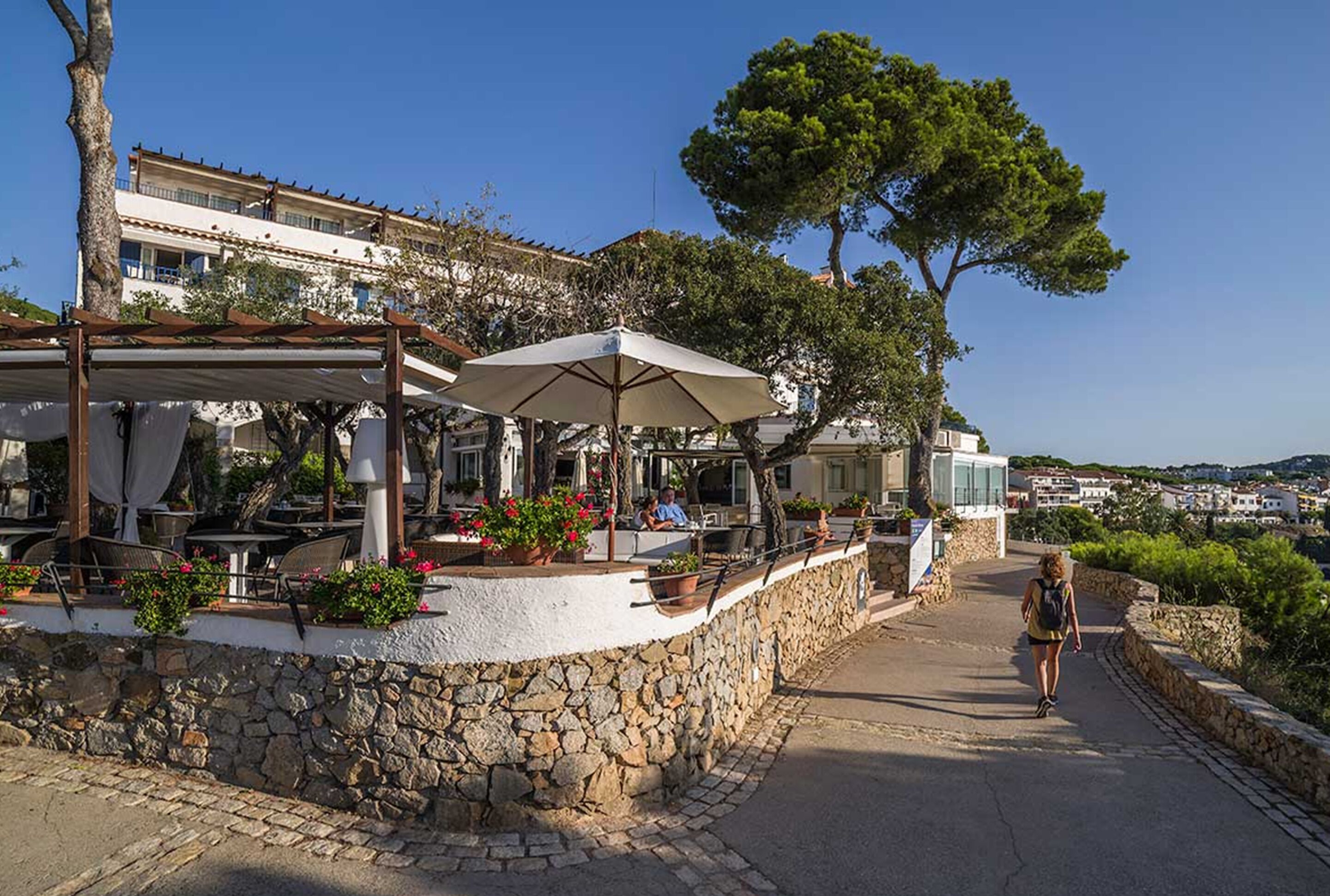Un café en plein air avec des murs en pierre, des tables à l’extérieur et des parasols.