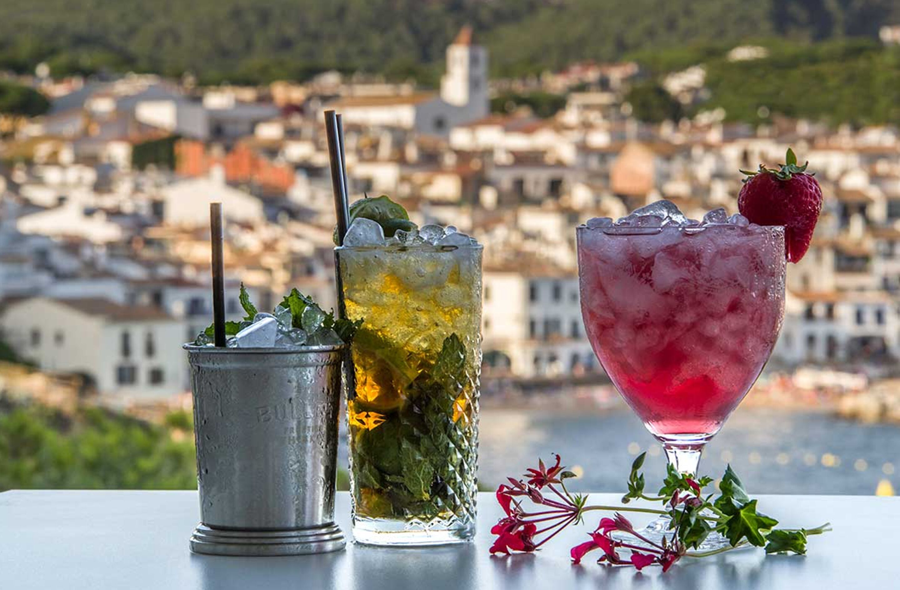 Three drinks on a table with a cityscape in the background.