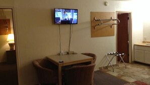 A small room with a television mounted on the wall, a table with two chairs, a small stool, and a door leading to a kitchenette. - Front Street Inn (Crescent City)