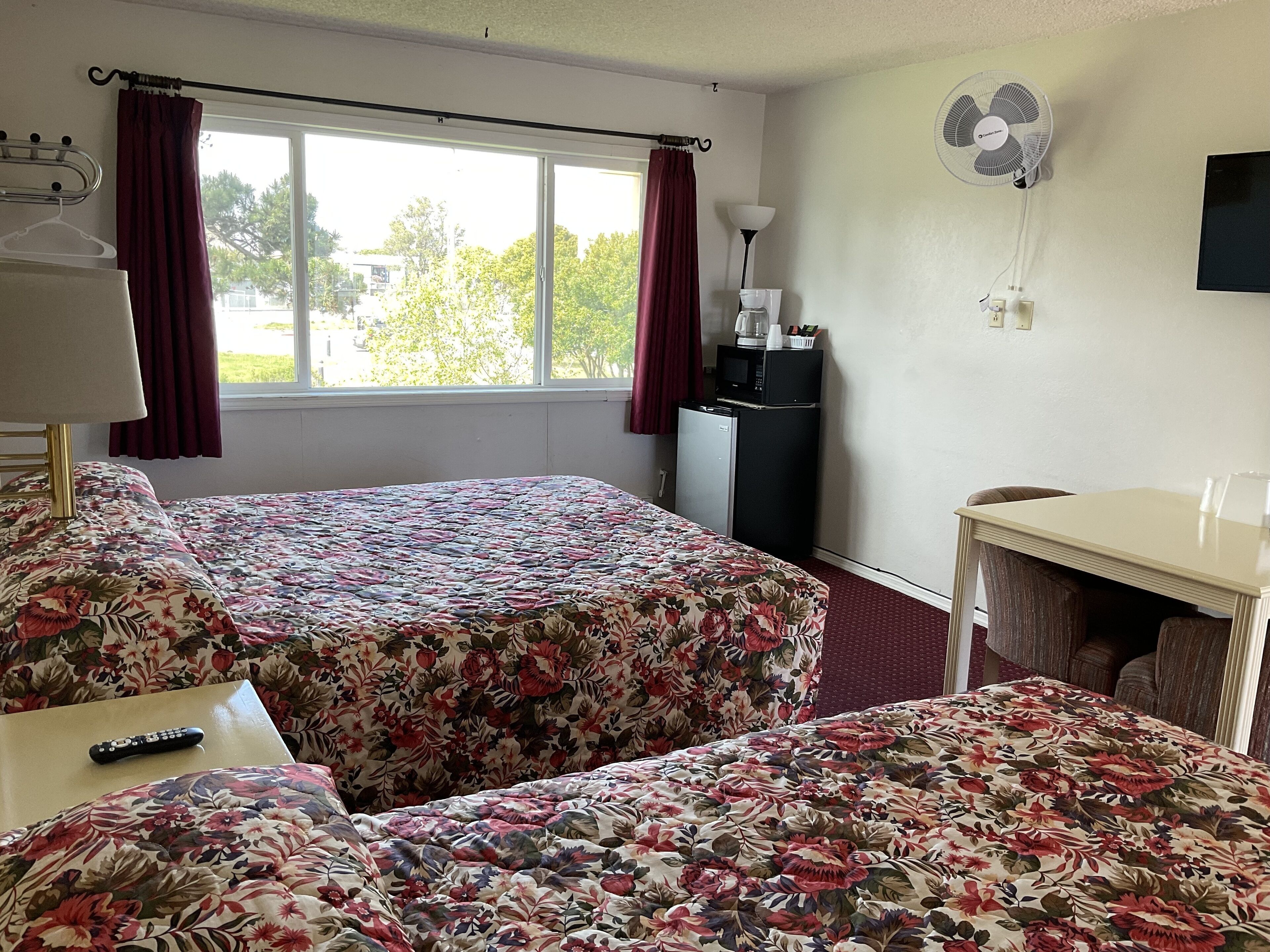A hotel room with two beds, a desk, a chair, a TV, a microwave, and a window with curtains.