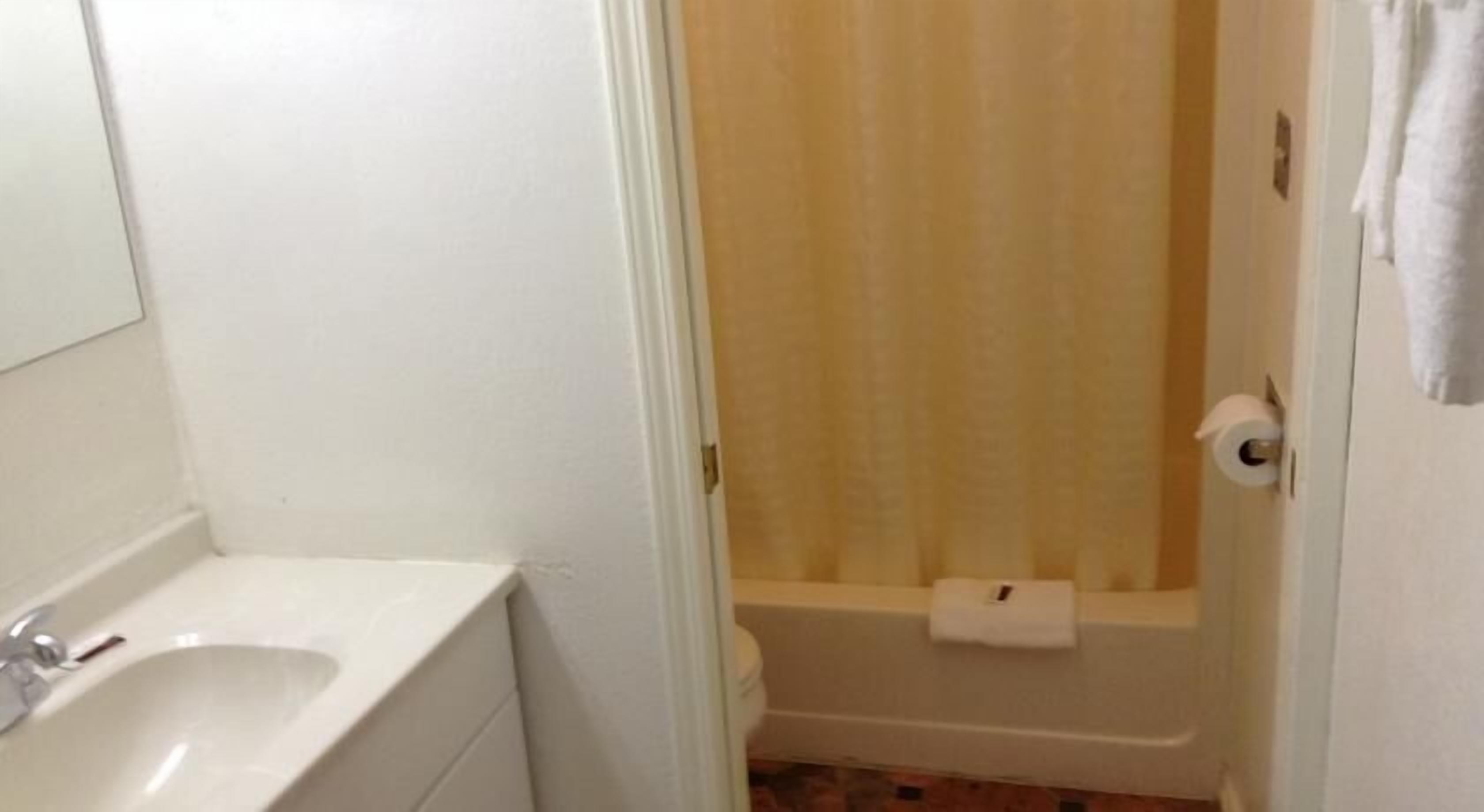 A bathroom with a white sink, a shower with a beige curtain, and a toilet.