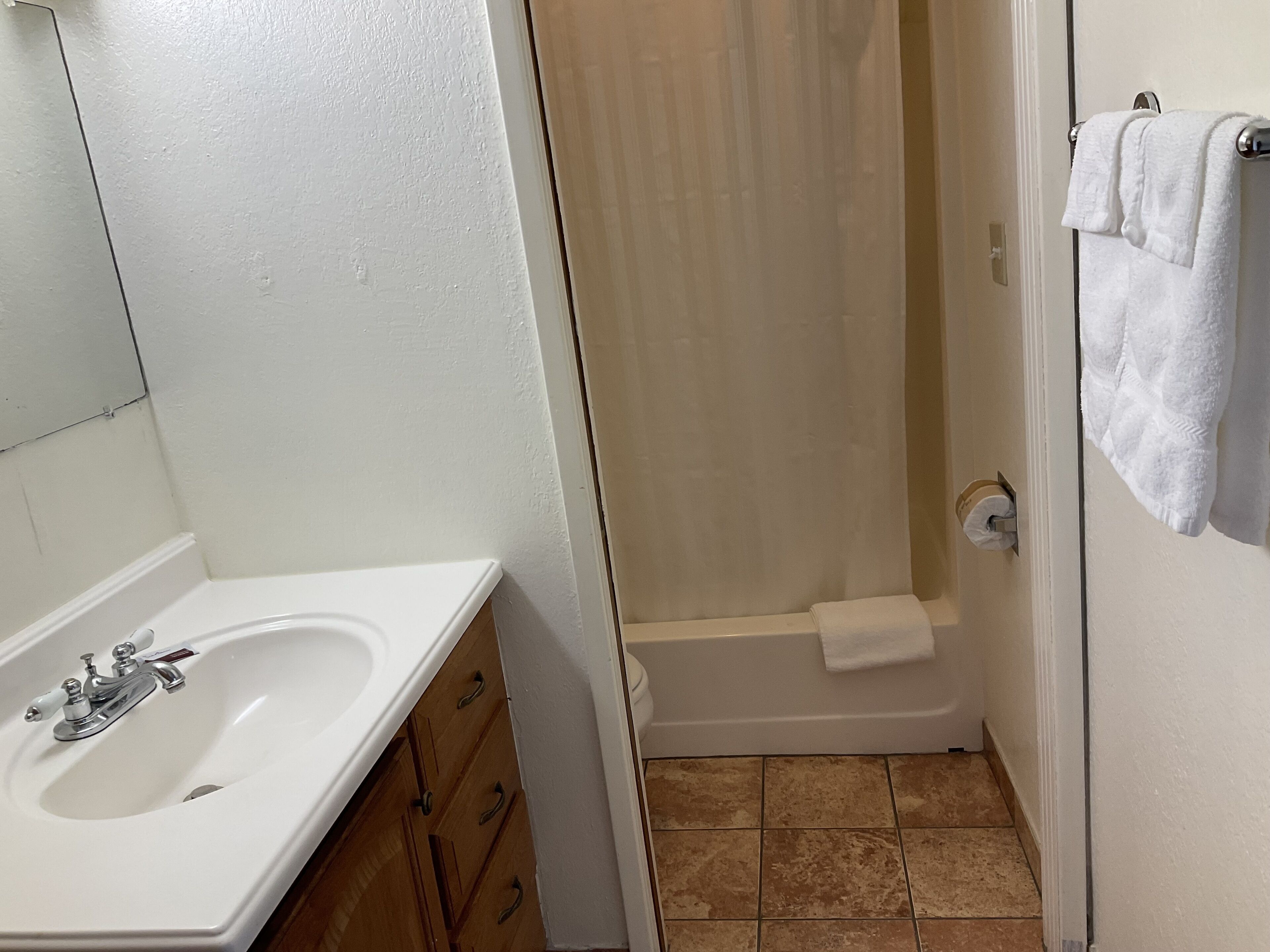 Un baño con lavamanos blanco, armarios de madera, cortina de ducha y toallero.