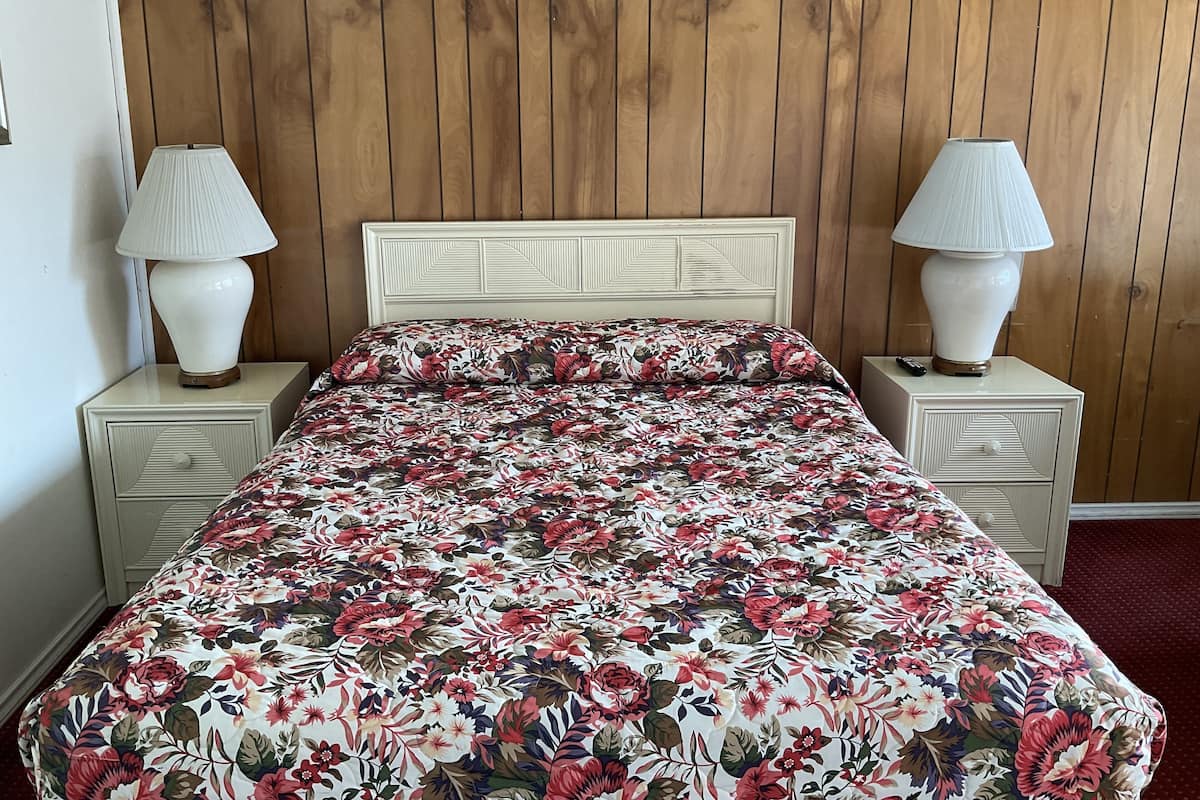 A bed with a floral bedspread, two bedside lamps, and a wooden headboard.