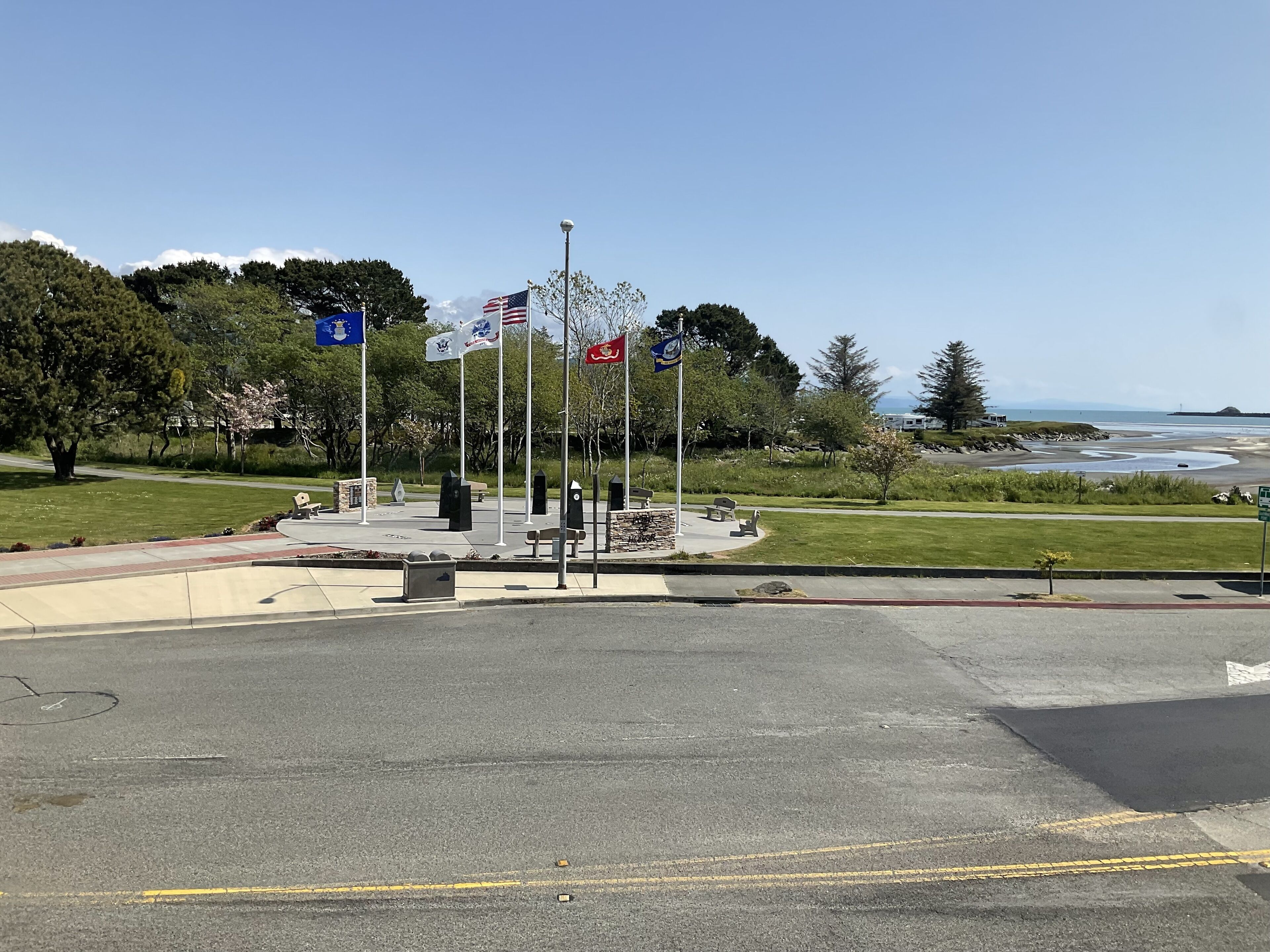 A parking lot with multiple flags, a grassy area, and a view of the ocean.