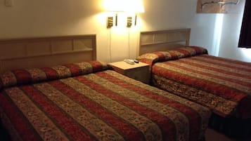 Una habitación de hotel con dos camas, cada una con colcha estampada, una mesita de noche con lámpara y una lámpara de pared.