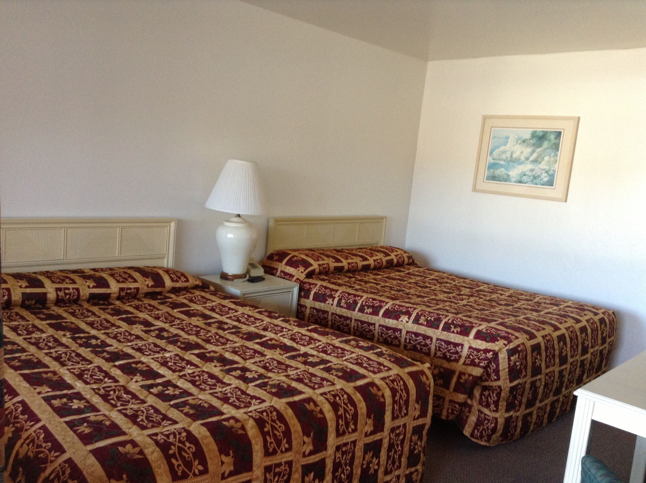 Habitación de hotel con dos camas individuales, una mesita de noche con lámpara y un cuadro enmarcado en la pared.