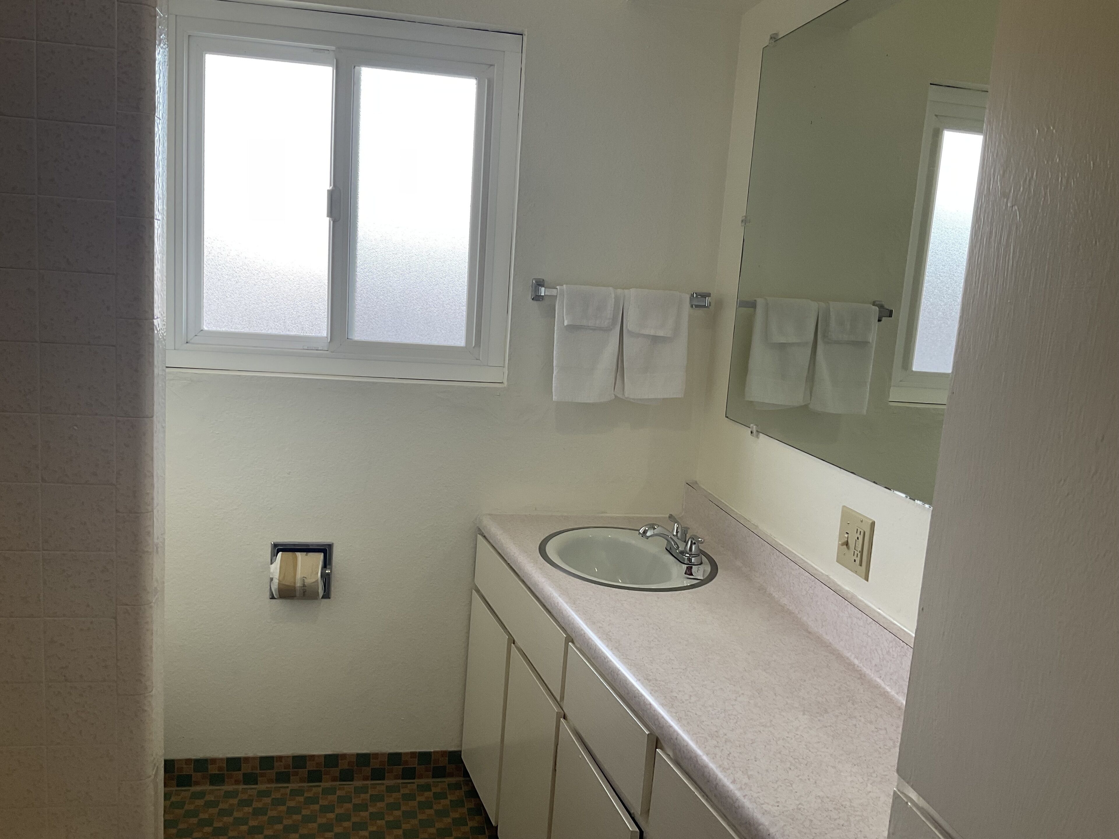 A small bathroom with a window, a sink, and a mirror.