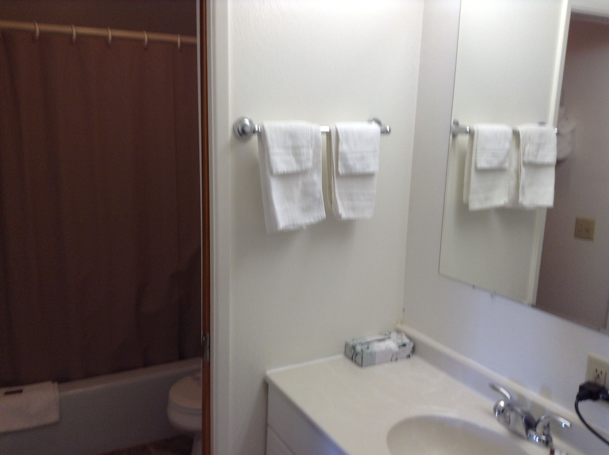 A bathroom with a shower curtain, a toilet, a sink with a mirror, and two towels hanging on a rack.