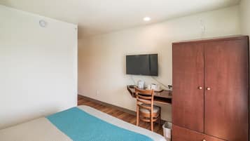 A hotel room with a bed, a desk with a chair, a television, and a wardrobe.