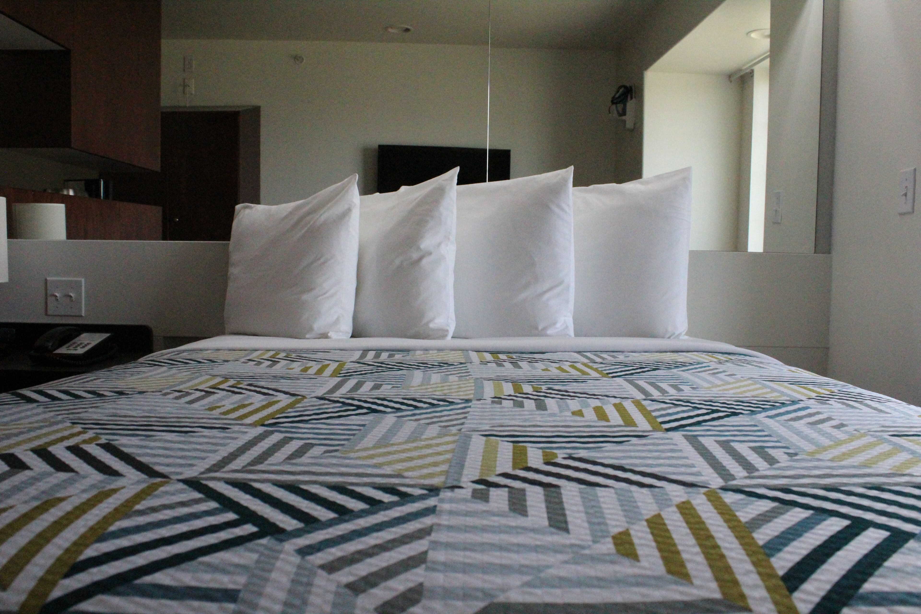 A hotel room with a bed, a nightstand, a telephone, and a mirror.