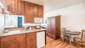 A compact kitchen with wooden cabinets, a microwave, a small refrigerator, a sink, and a dining area with two chairs. - Motel 6 Idaho Falls, ID - Snake River (Idaho Falls)