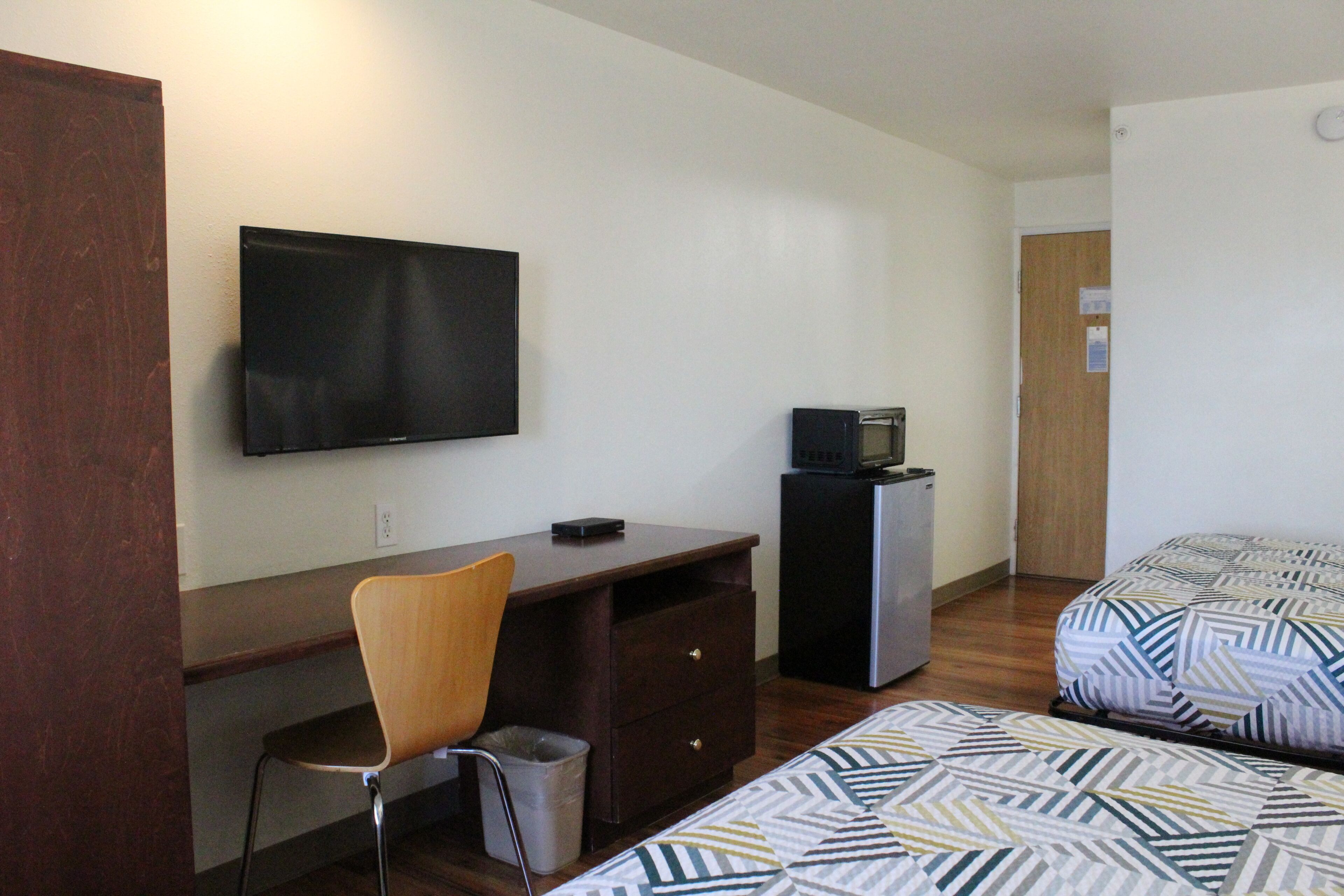 Una habitación con una cama, un escritorio, una silla, un televisor y un refrigerador pequeño.