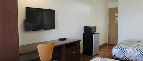 Una habitación con una cama, un escritorio, una silla, un televisor y un refrigerador pequeño.