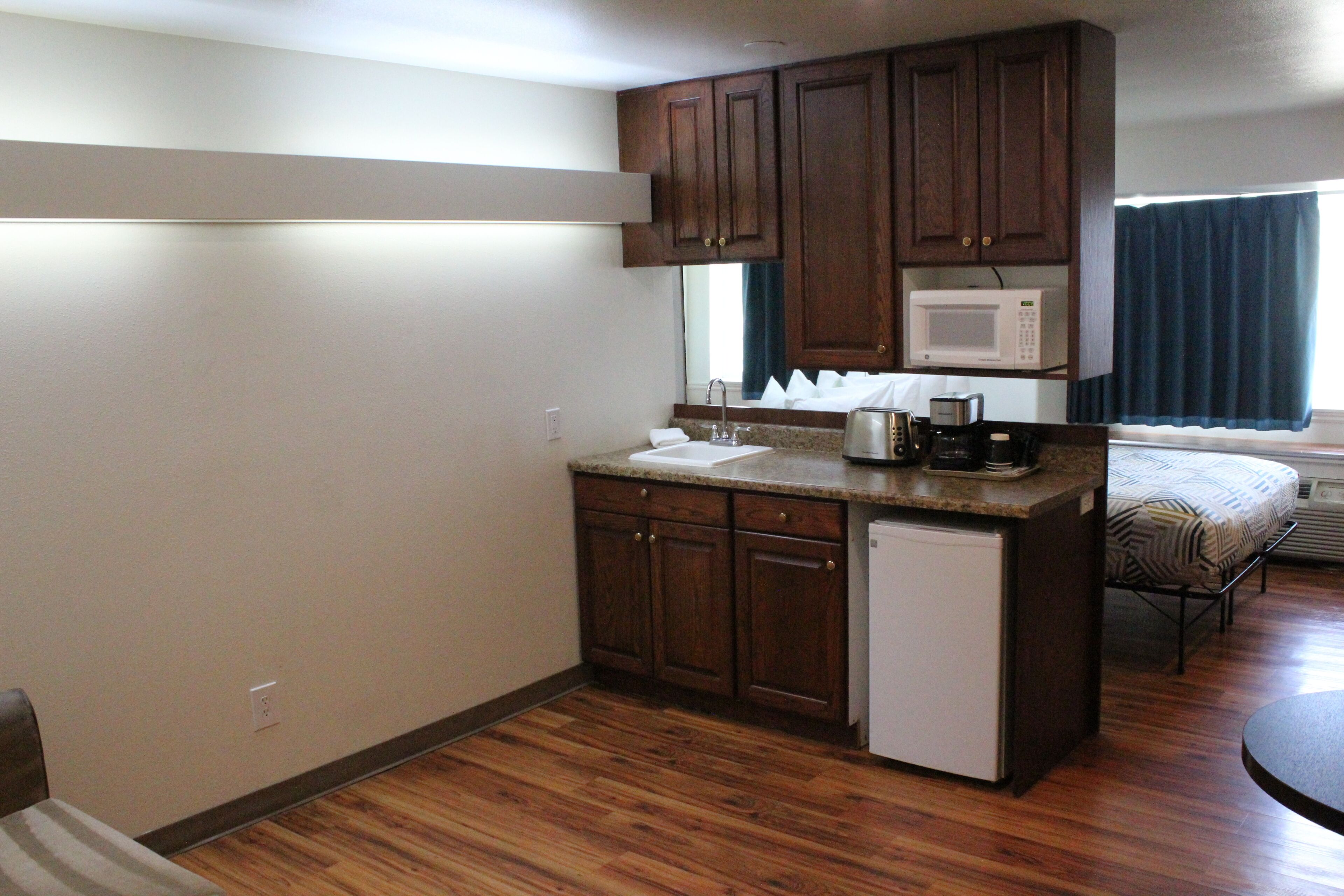 A compact kitchen with wooden cabinets, a microwave, a sink, and a small refrigerator.