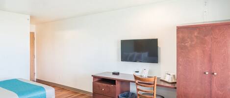 A hotel room with two beds, a desk with a television, a wardrobe, and a chair.