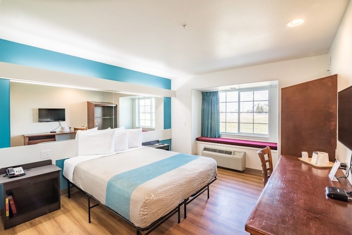 Habitación de hotel con cama, mesita de noche, escritorio, silla, ventana y televisor de pantalla plana.
