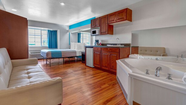 A modern room with a sofa, a small kitchenette, a bathtub, and a window with curtains. - Motel 6 Idaho Falls, ID - Snake River (Idaho Falls)