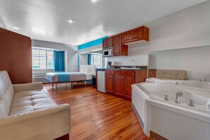 Une chambre moderne avec un canapé, une petite kitchenette, une baignoire et une fenêtre avec des rideaux.